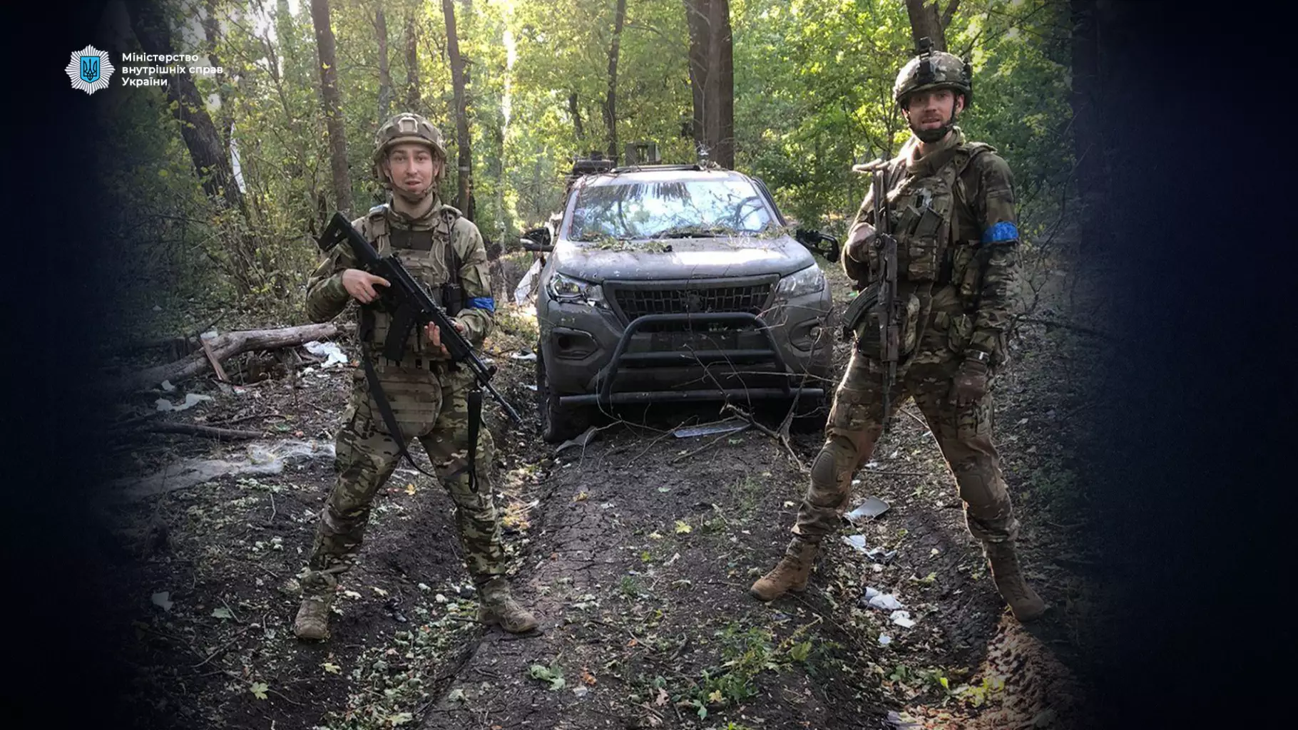 Двоє українських прикордонників у військовій формі стоять перед позашляховиком у лісі