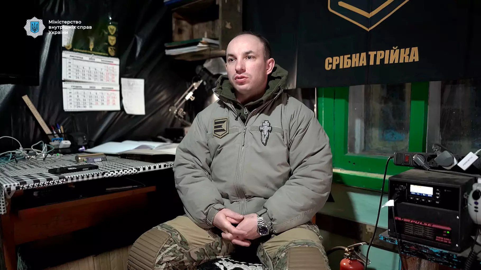 Прикордонник у зимовій формі сидить у штабі, на стіні прапор з написом "Срібна трійка