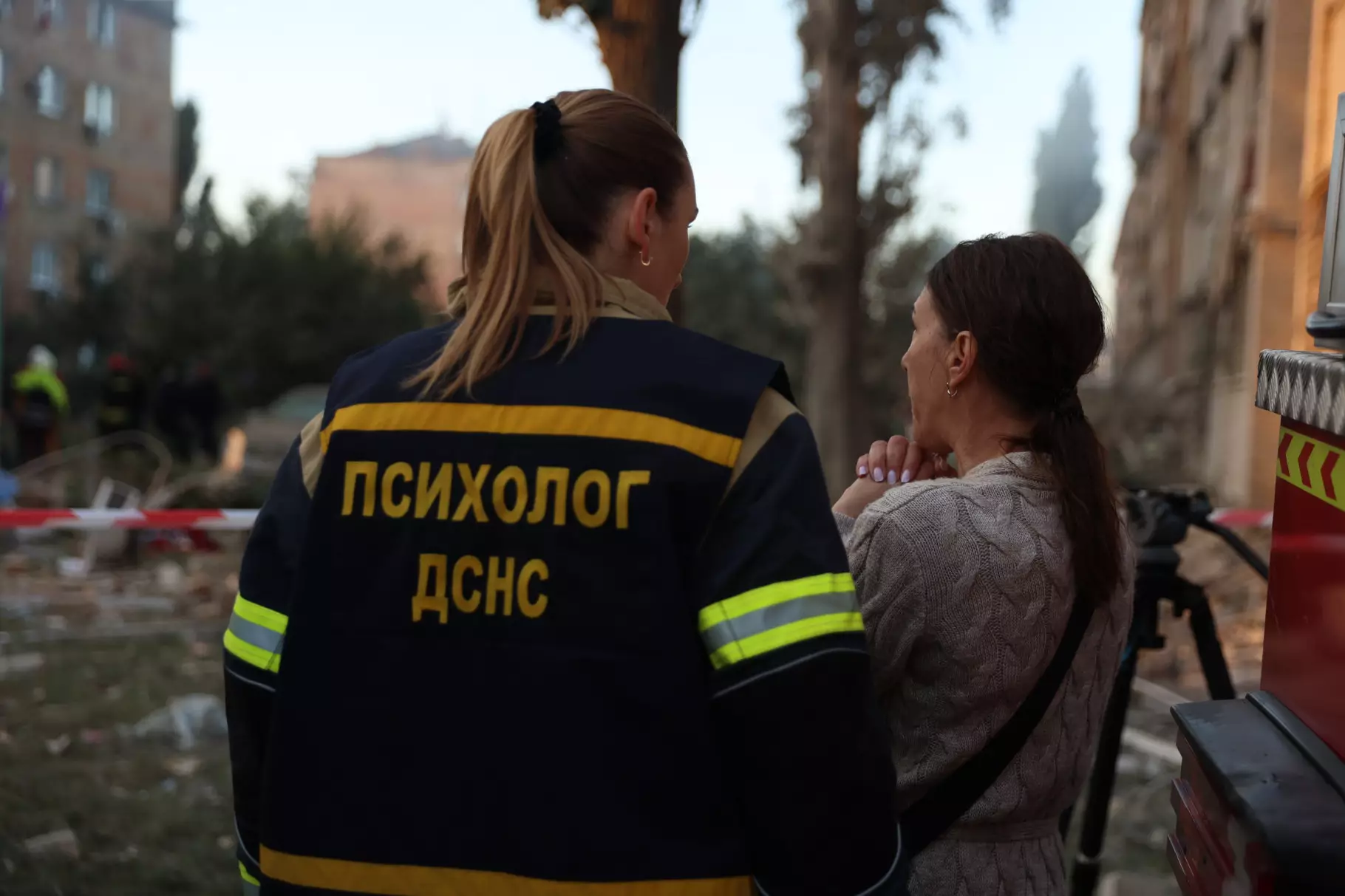 Психолог ДСНС надає підтримку жінці на місці обстрілу, пошкоджені будівлі на задньому плані