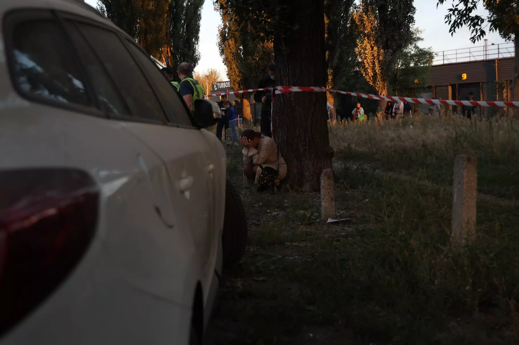 Люди біля дерева під час заходу безпеки, автомобіль на передньому плані, стрічка огороджує місце події