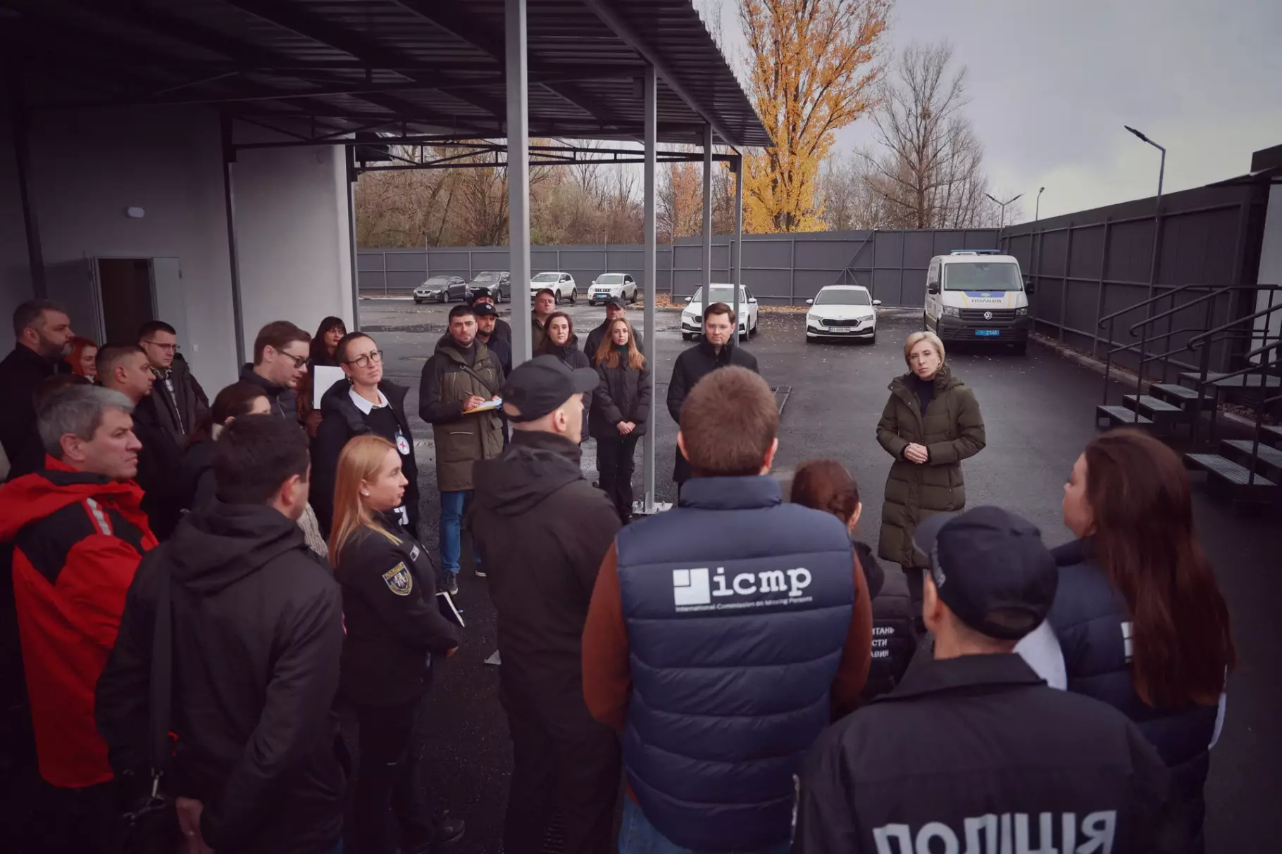 Група людей у формі обговорює питання безпеки на відкритому майданчику біля поліцейських автомобілів