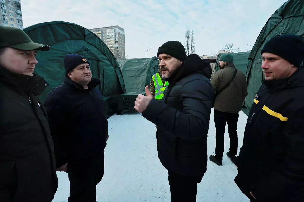 Люди в зимовому одязі обговорюють розгортання наметів обігріву на засніженій території біля багатоповерхівок