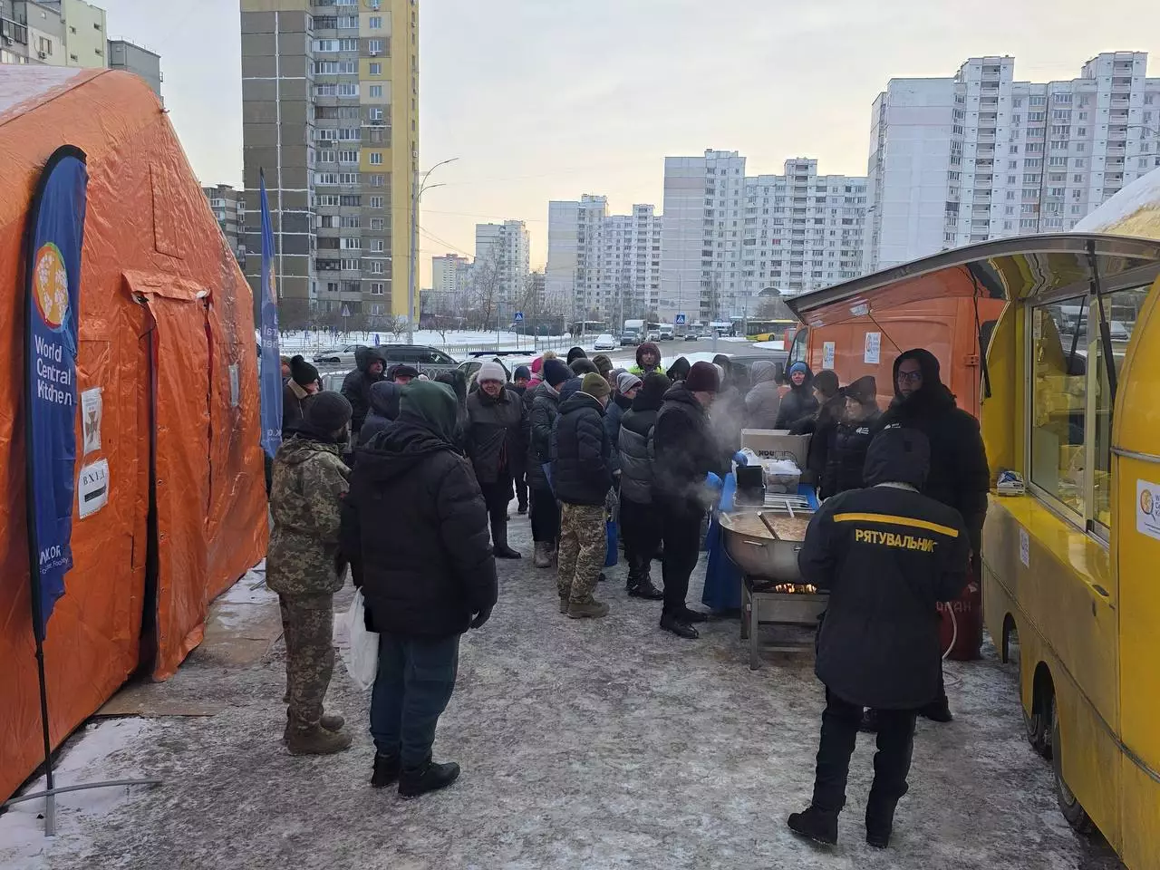 Люди зібралися біля наметів обігріву та мобільної кухні в зимовому Києві, отримують гарячу їжу