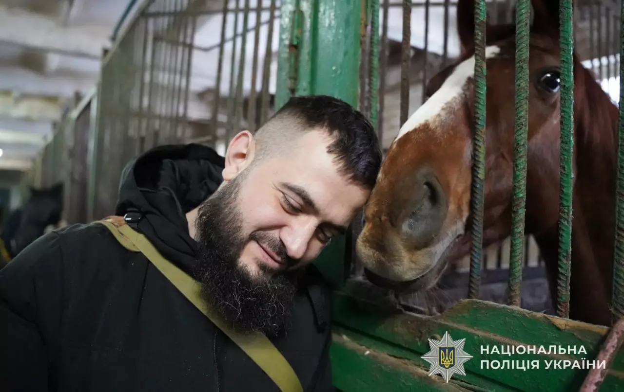 Чоловік у військовій формі спілкується з конем у стайні, демонструючи довіру та спокій