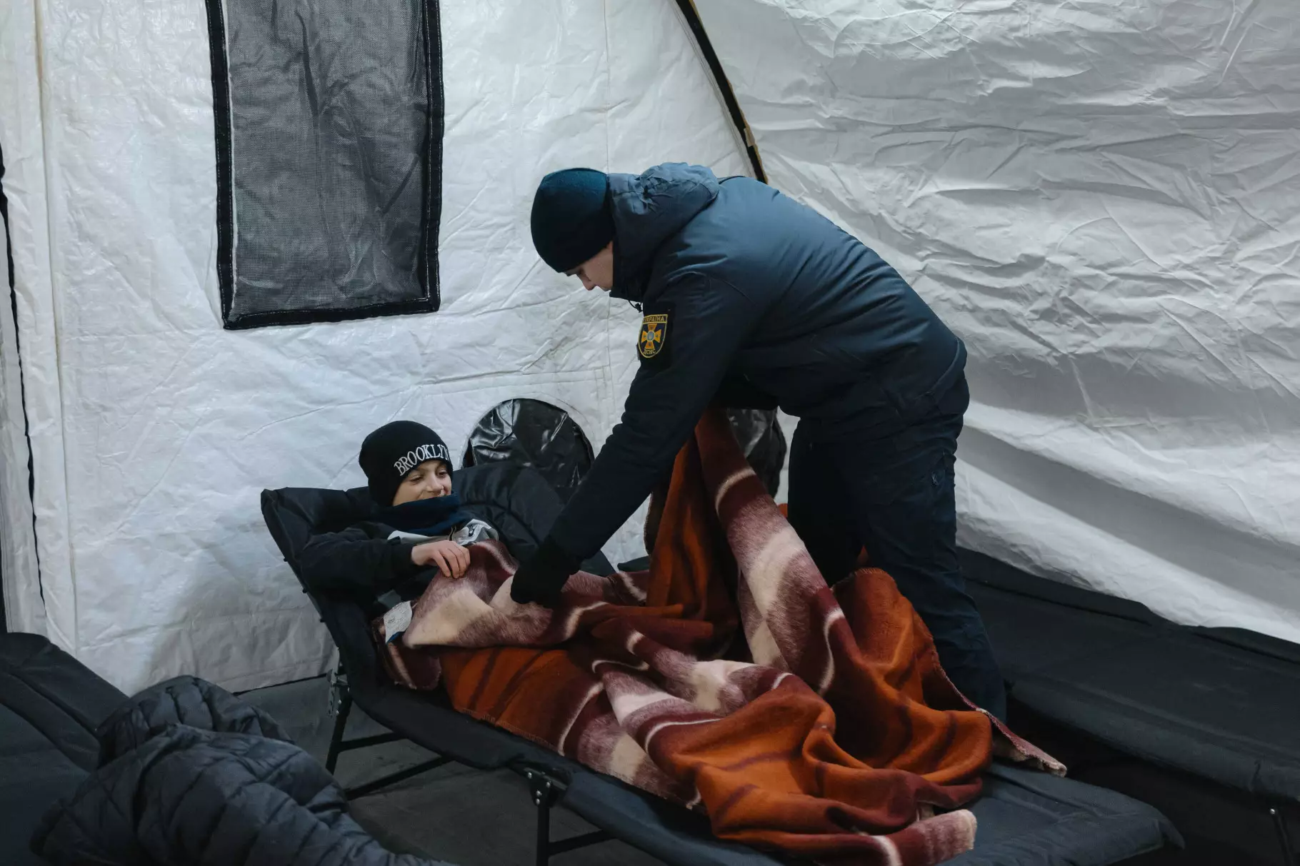 Рятувальник ДСНС України накриває ковдрою дитину в наметовому містечку на Троєщині після обстрілу