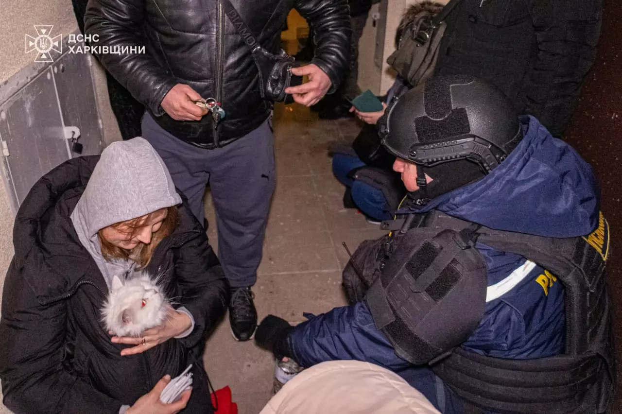 Люди в укритті під час обстрілу, рятувальник у шоломі допомагає жінці з котом на руках