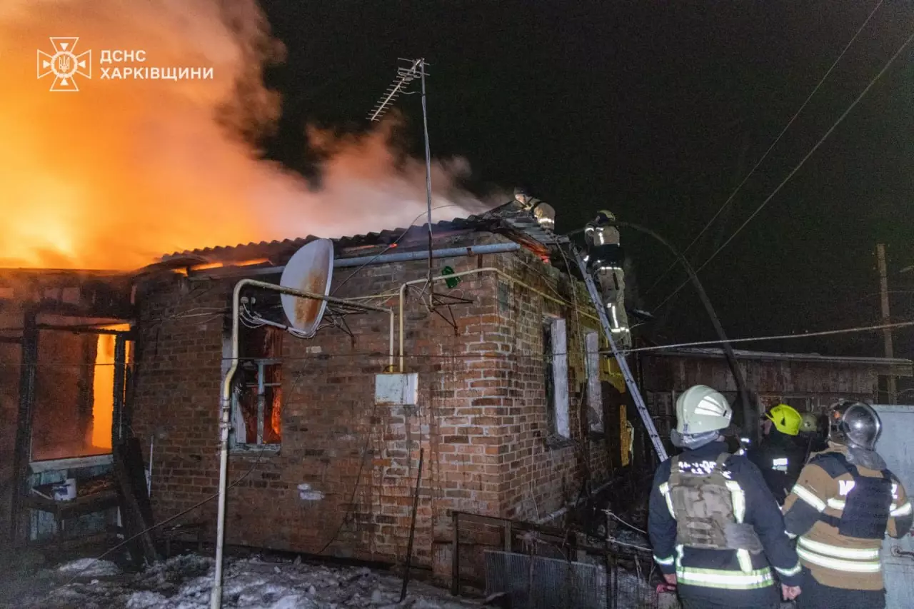 Пожежники гасять вогонь на даху пошкодженого будинку вночі після обстрілу в Харківській області