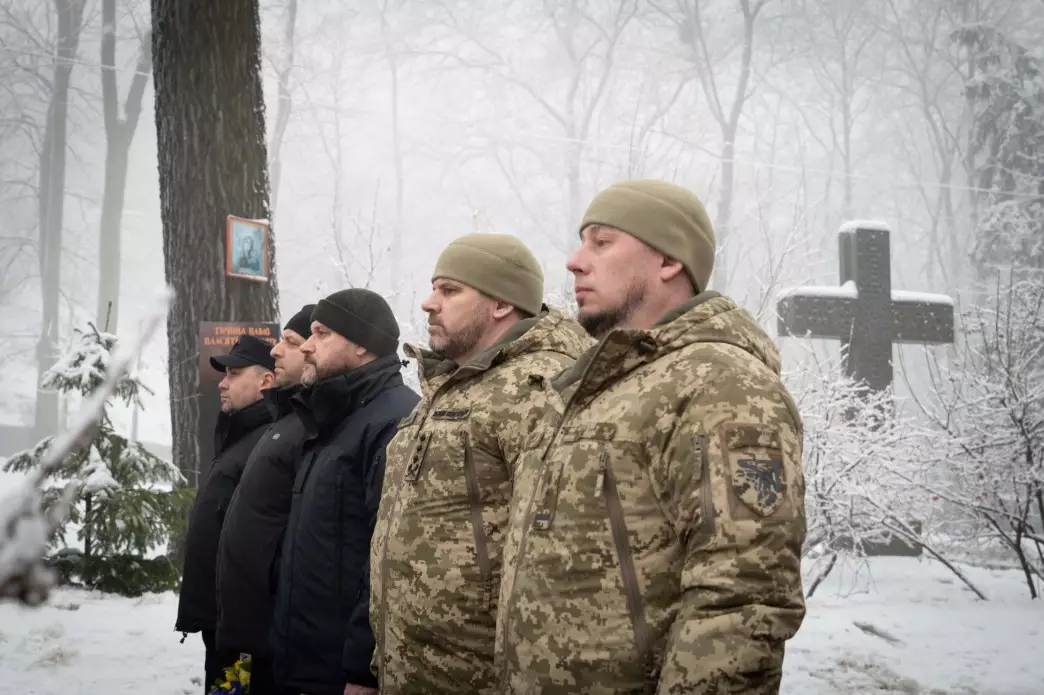 Чоловіки в камуфляжі та цивільному одязі стоять біля пам'ятного хреста на Аскольдовій могилі в Києві