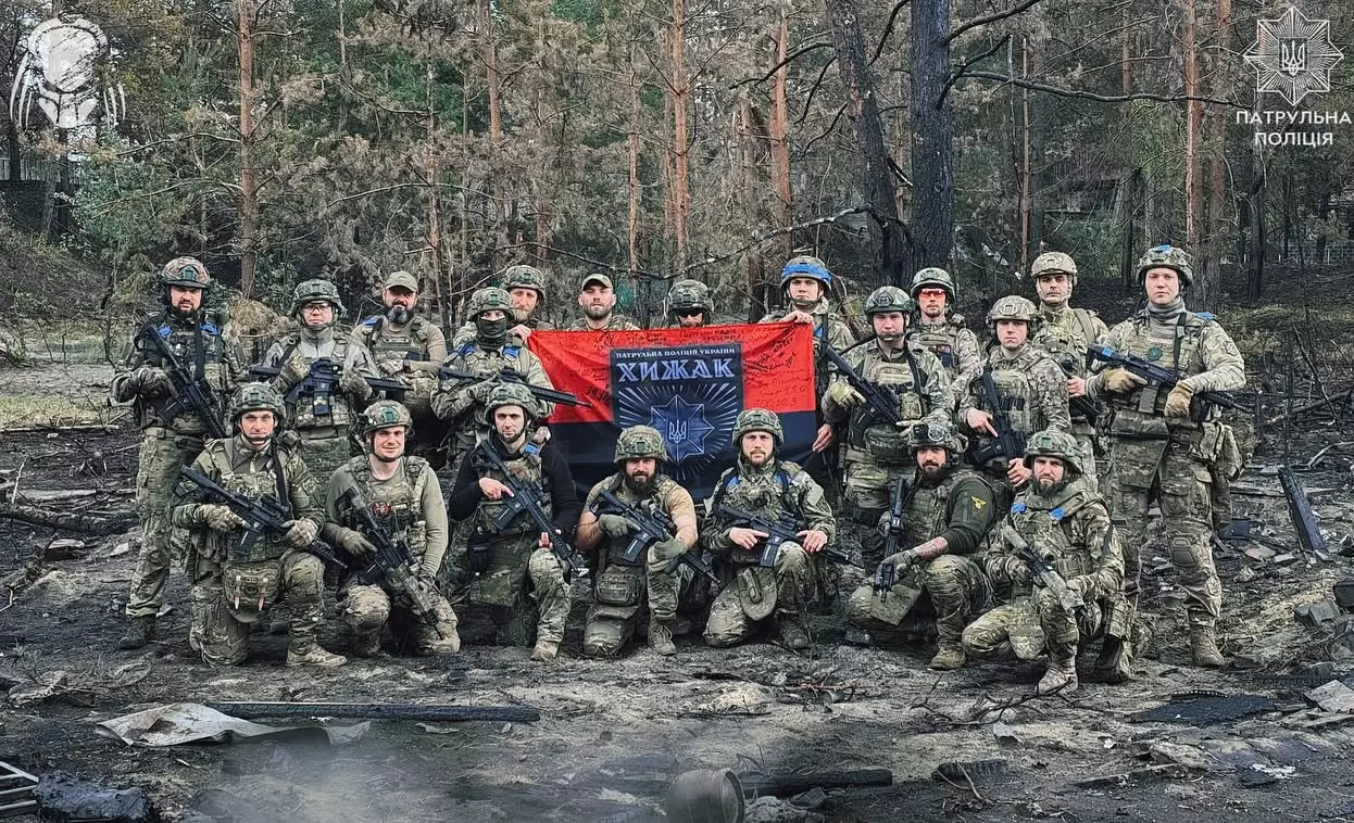 Група військових у камуфляжі з прапором на фоні лісу, символіка Національної поліції України