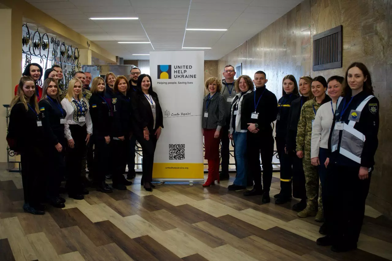 Учасники тренінгу УП+ у МВС України стоять біля банера United Help Ukraine у приміщенні навчального центру
