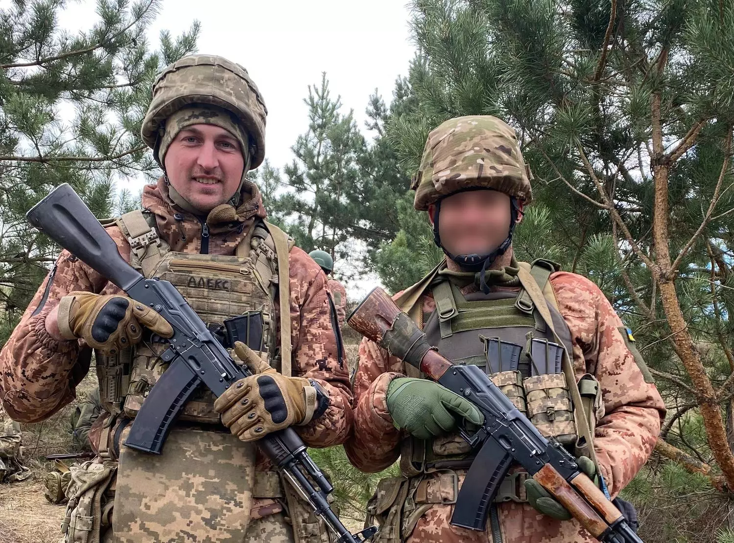 Двоє військових у камуфляжі з автоматами на фоні соснового лісу, усміхнені та готові до дії