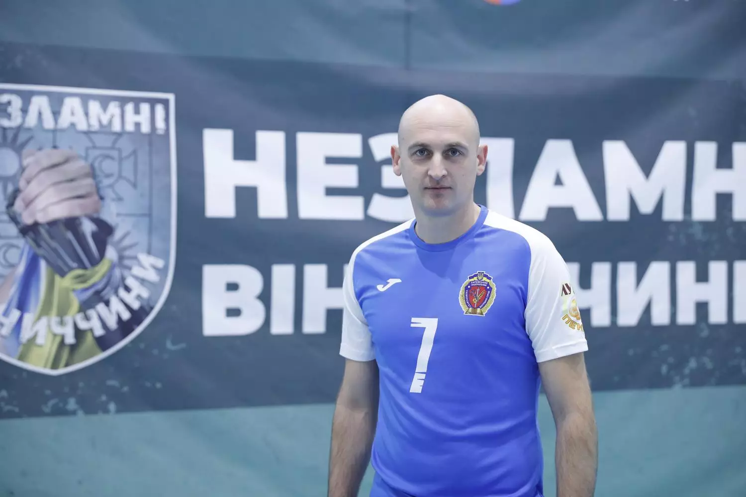 Ветеран у синій спортивній формі стоїть на фоні банера з написом "Незламні