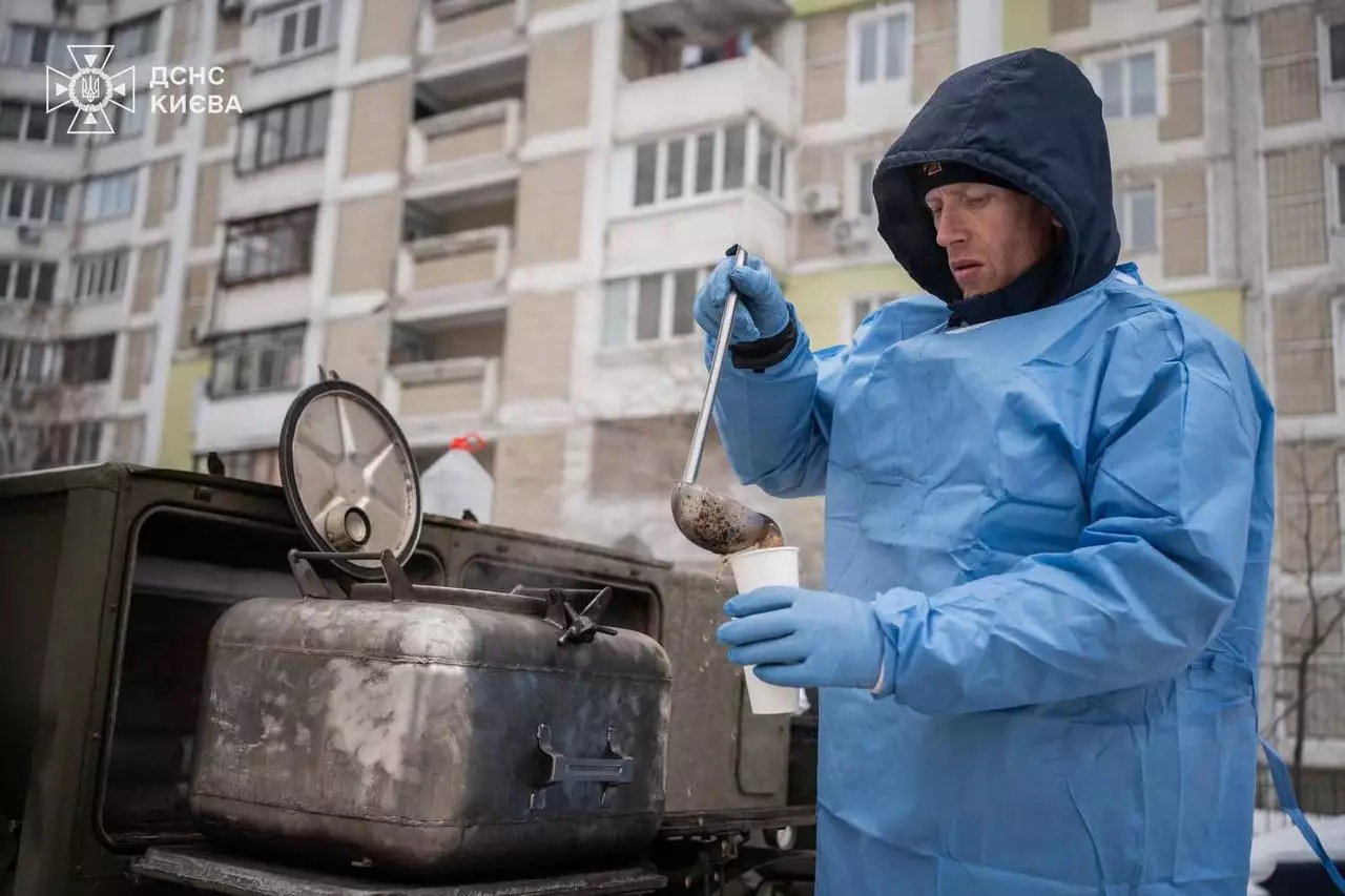 Рятувальник у синьому захисному одязі наливає гарячий напій у дворі багатоповерхівки