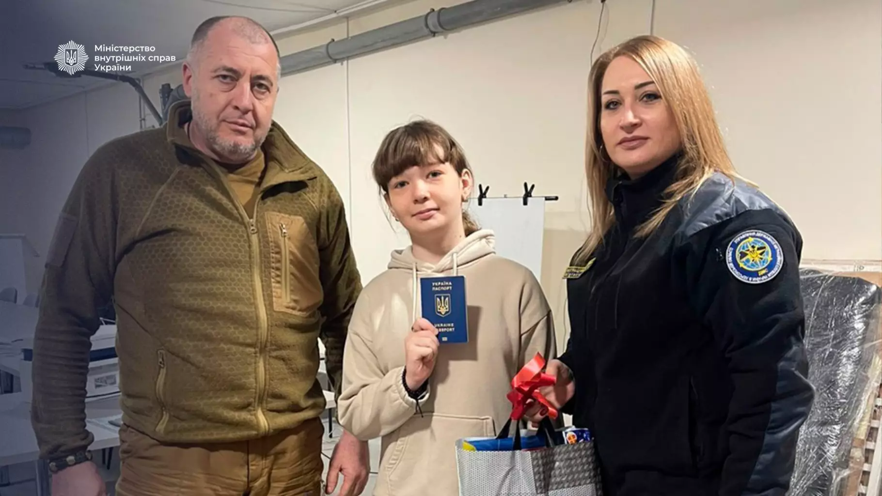 Троє людей у приміщенні, дитина тримає паспорт України, працівники ДМС поруч