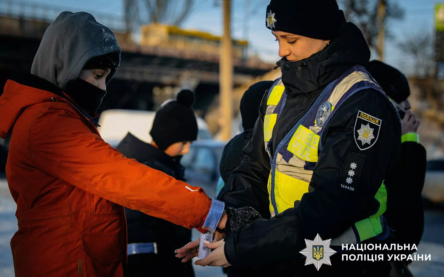 Ювенальний поліцейський одягає світловідбивальний браслет на руку дитині в зимовому одязі