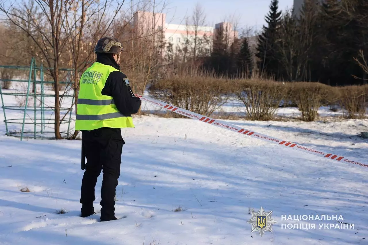 Поліцейський оглядає місце обстрілу в зимовому парку, оточене стрічкою, Київщина, лютий 2026
