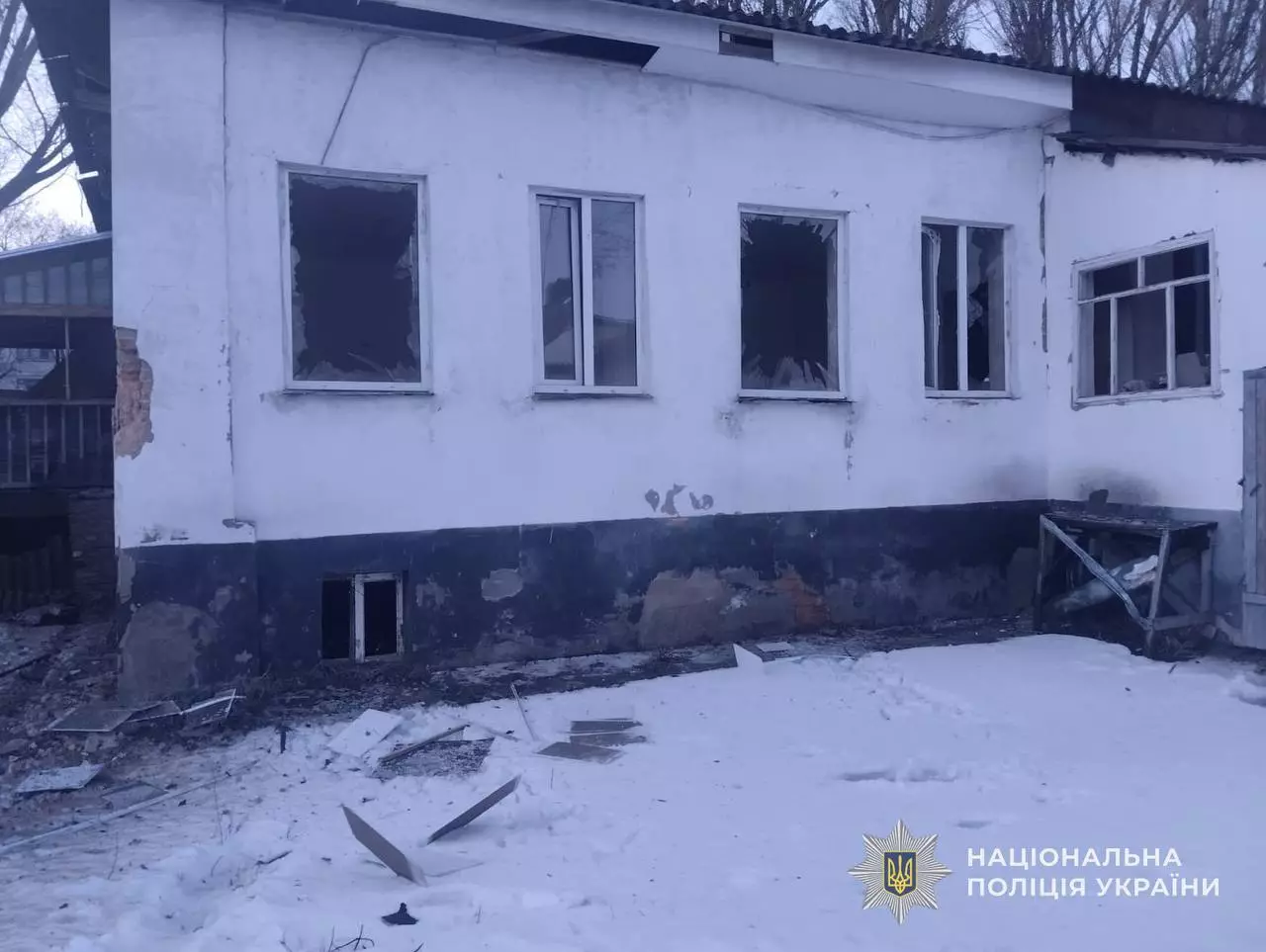 Пошкоджена будівля з вибитими вікнами після обстрілу, сніг на землі, робота поліції України