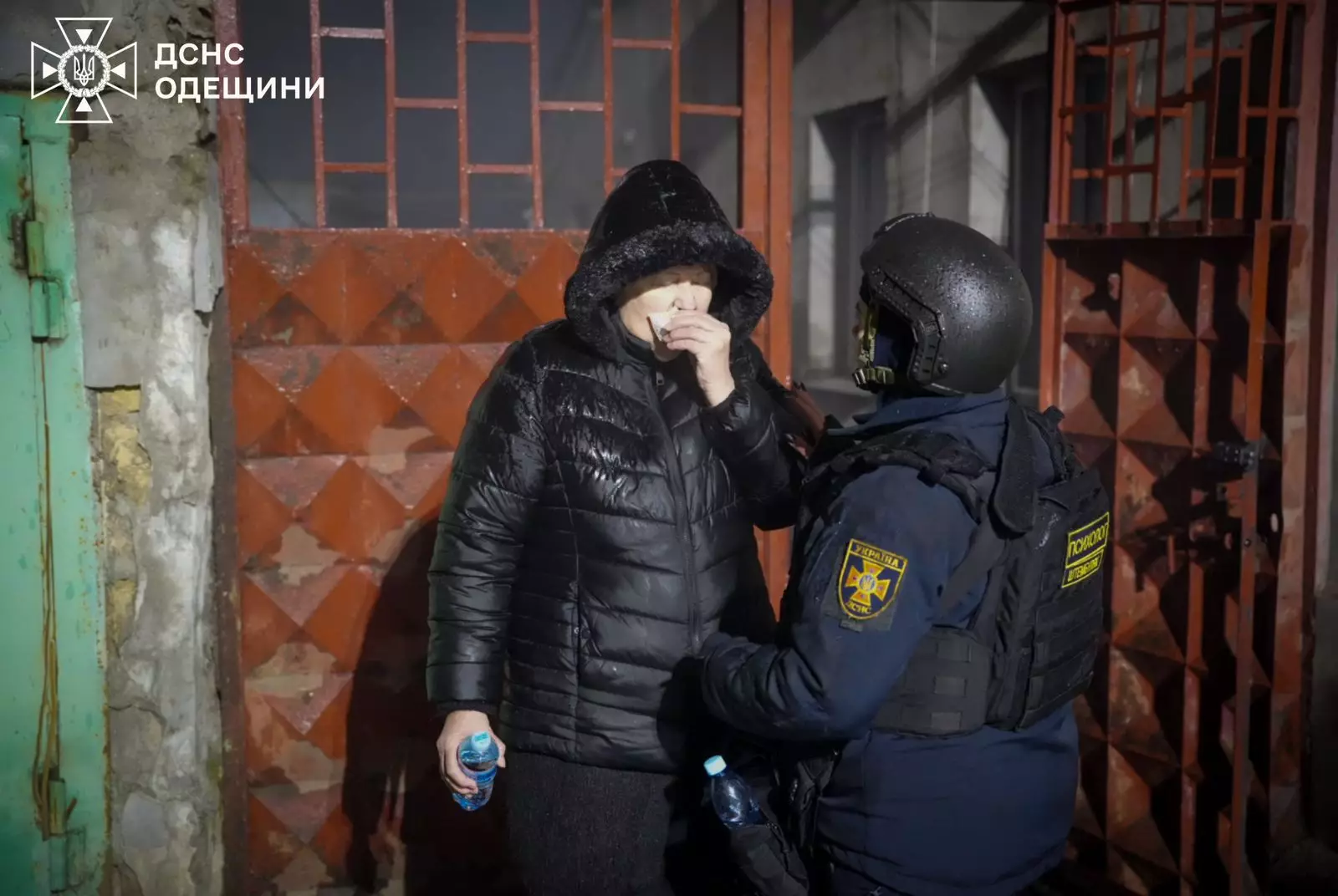 Поліцейський надає допомогу жінці біля пошкодженого будинку після обстрілу в Одеській області