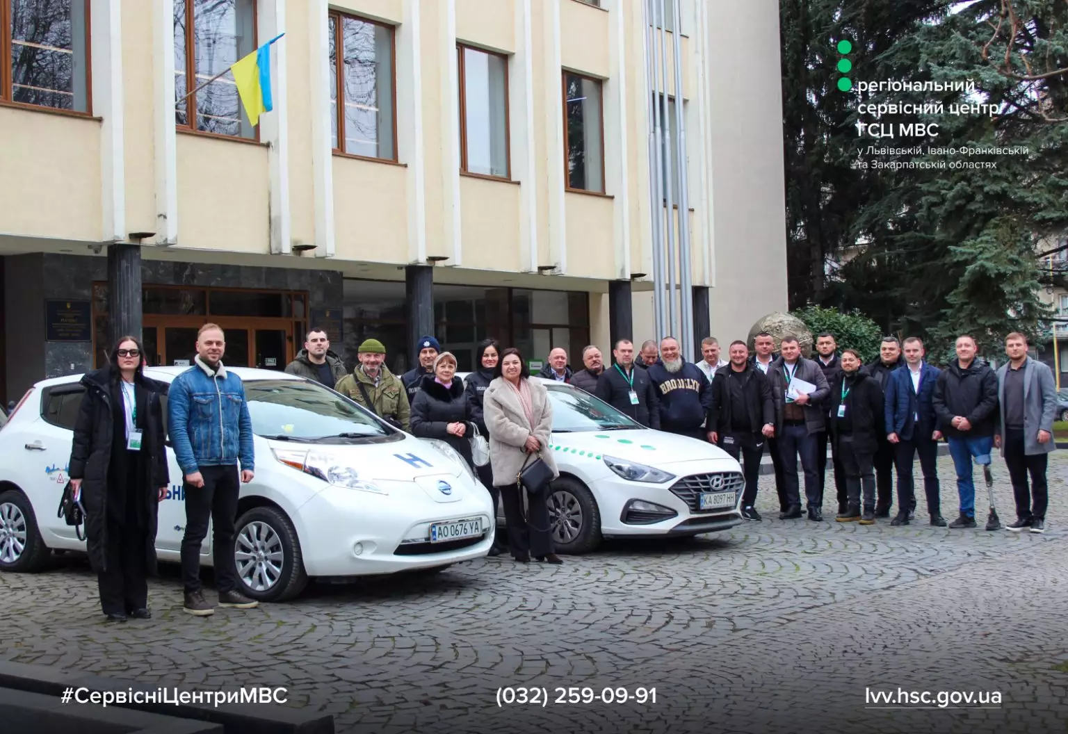 Група людей біля двох автомобілів на тлі будівлі, учасники заходу з інклюзивної мобільності