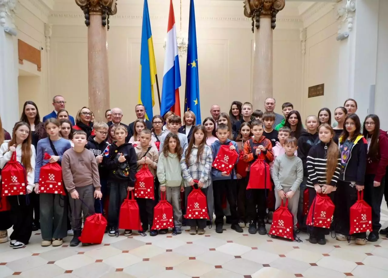 Діти з України з подарунковими пакетами стоять перед прапорами України, Хорватії та ЄС у Загребі