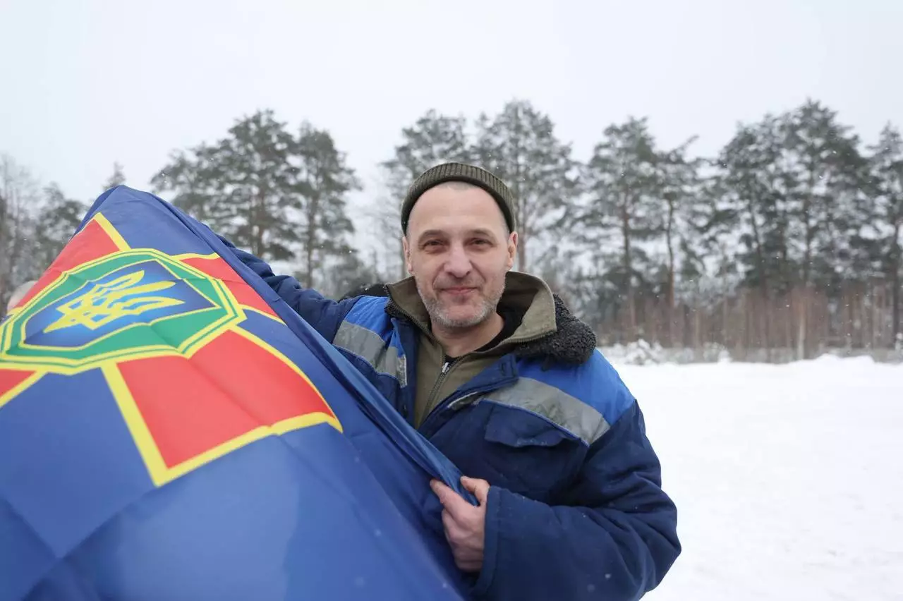 Чоловік у зимовому одязі тримає прапор України на фоні засніженого лісу