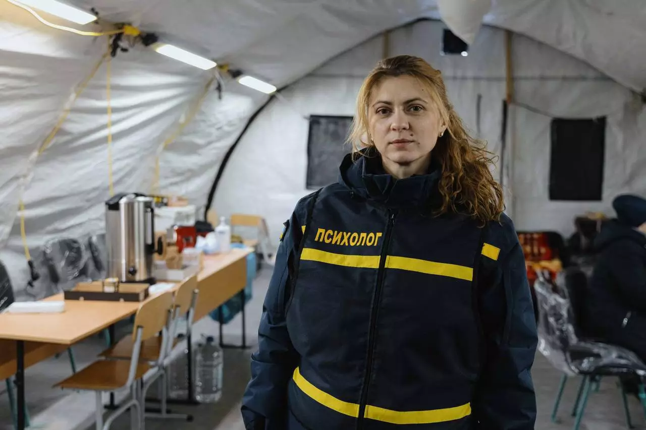 Жінка у формі психолога стоїть всередині намету обігріву з обладнанням для допомоги людям