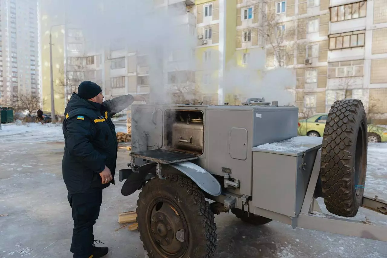 Рятувальник біля мобільної пічки в пункті обігріву на тлі багатоповерхівок взимку