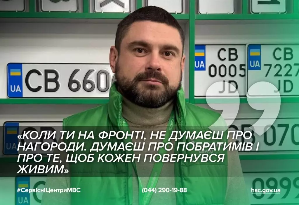 Чоловік у зеленій жилетці стоїть перед стіною з номерними знаками в сервісному центрі МВС