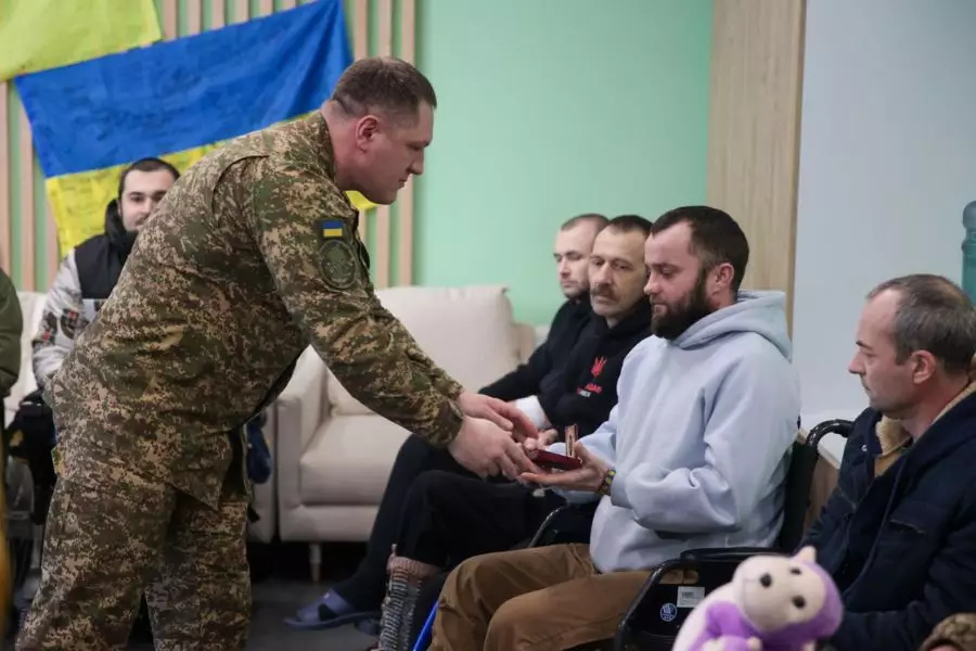 Командувач НГУ вручає нагрудний знак пораненому нацгвардійцю в лікарні, поруч інші військові