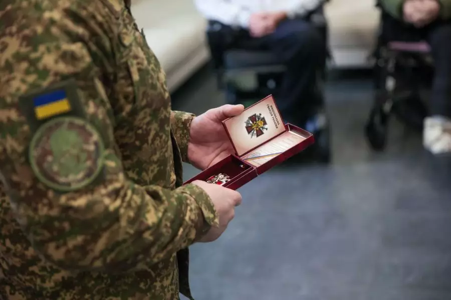 Військовослужбовець у формі тримає нагороду в червоній коробці під час зустрічі з пораненими воїнами