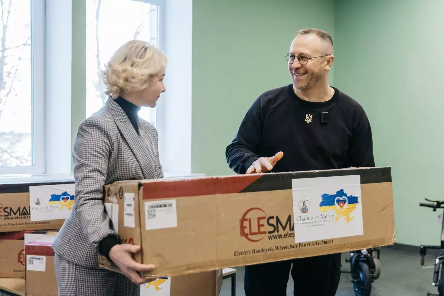 Двоє людей тримають коробку з електроприводом для крісла колісного в медичному центрі