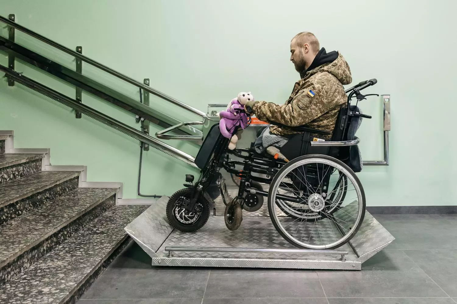 Чоловік у військовій формі на інвалідному візку з електроприводом піднімається пандусом