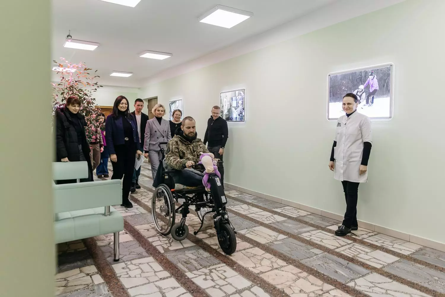 Чоловік у кріслі колісному з електроприводом у коридорі медичного центру, оточений медперсоналом