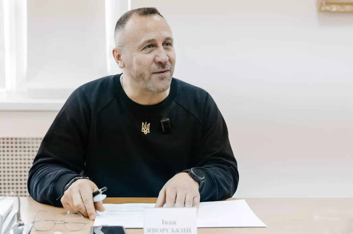 Чоловік у чорному светрі сидить за столом з документами, говорить про реабілітацію ветеранів МВС
