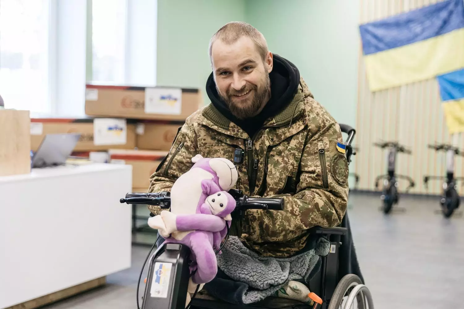 Ветеран у військовій формі на інвалідному візку з електроприводом, тримає м'яку іграшку