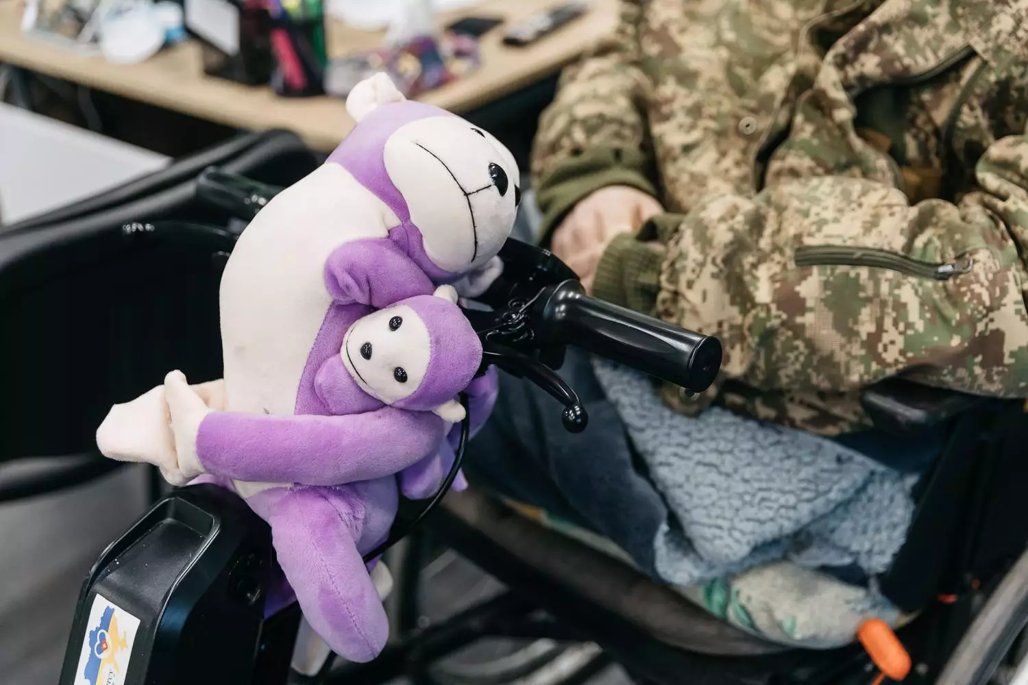 Військовий у камуфляжі на інвалідному візку з фіолетовими іграшками на ручці керма