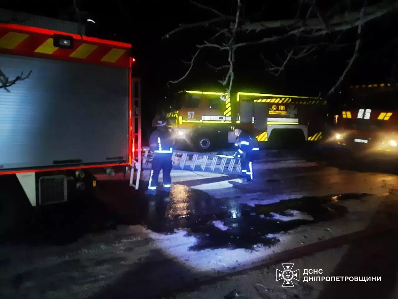 Рятувальники працюють біля пожежних машин уночі після обстрілів, освітлюючи місце події ліхтарями