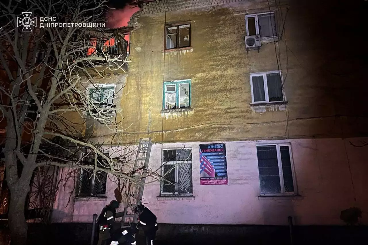Пожежники оглядають пошкоджений обстрілами житловий будинок у нічний час, видно сліди вогню