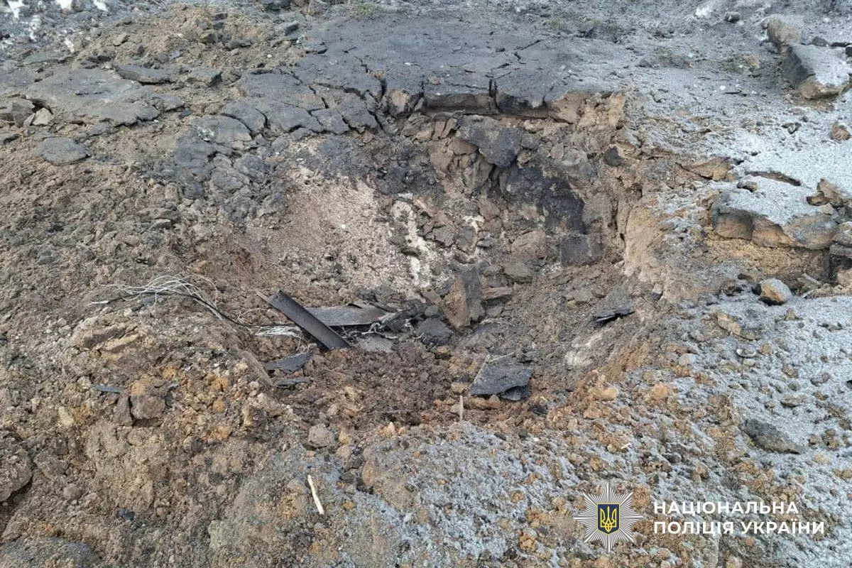 Воронка на асфальті після обстрілу, пошкоджена земля, уламки навколо, логотип Нацполіції України