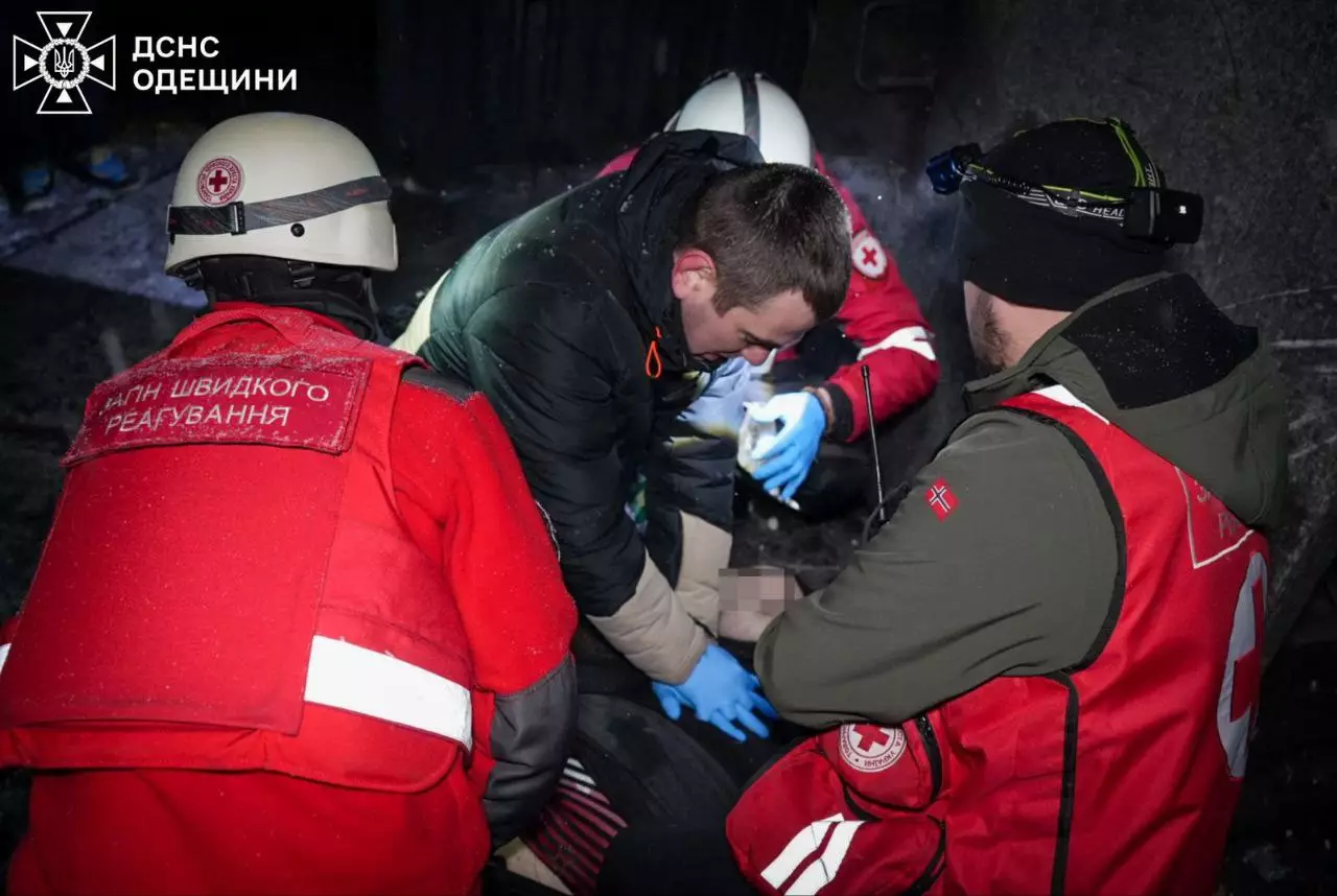 Рятувальники надають допомогу постраждалому після обстрілу в темряві, видно форму ДСНС та Червоного Хреста