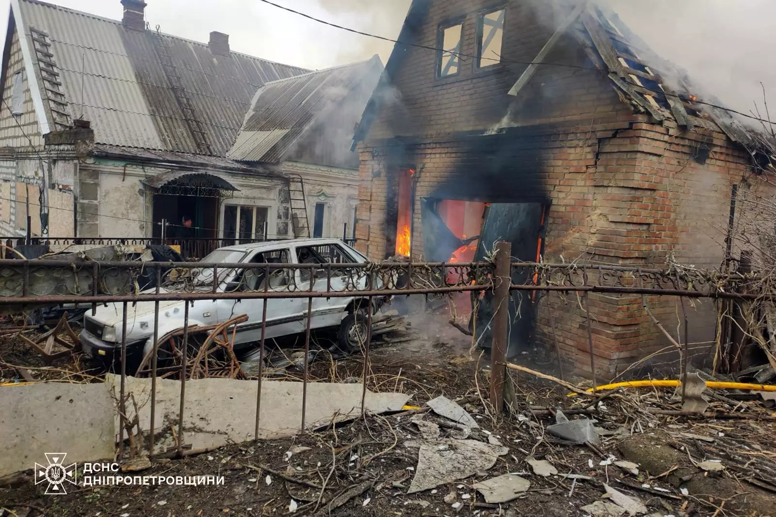 Пошкоджений будинок після обстрілу, поруч зруйнований автомобіль, видніються сліди пожежі