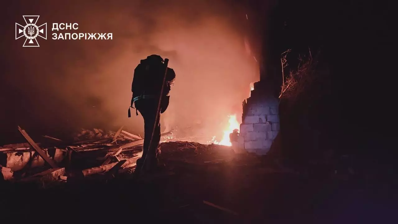 Рятувальник гасить пожежу вночі після атаки дронами в Запорізькій області, видно полум'я та руїни