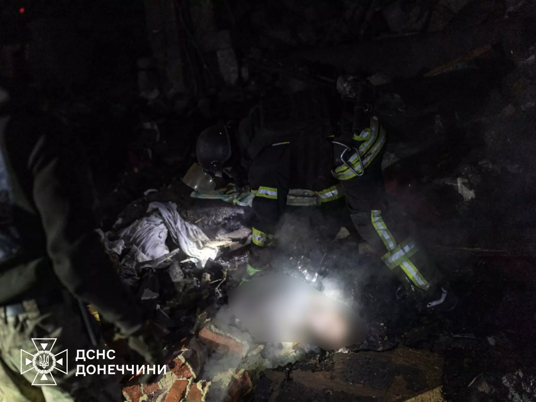 Рятувальники обстежують зруйновану будівлю вночі після обстрілу, дим і уламки навколо
