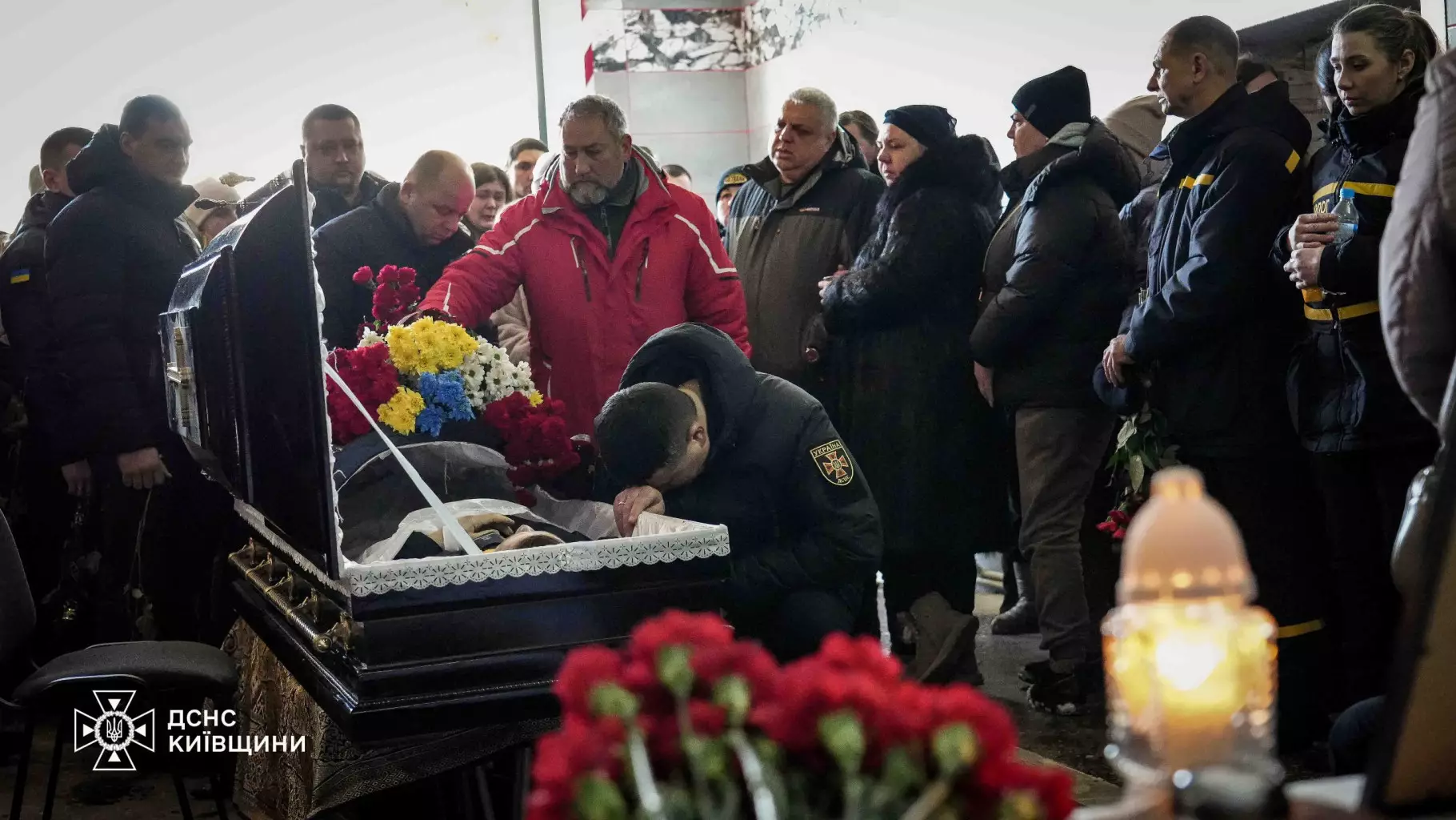 Люди прощаються з рятувальником Михайлом Проценком біля відкритої труни, оточені квітами та свічками