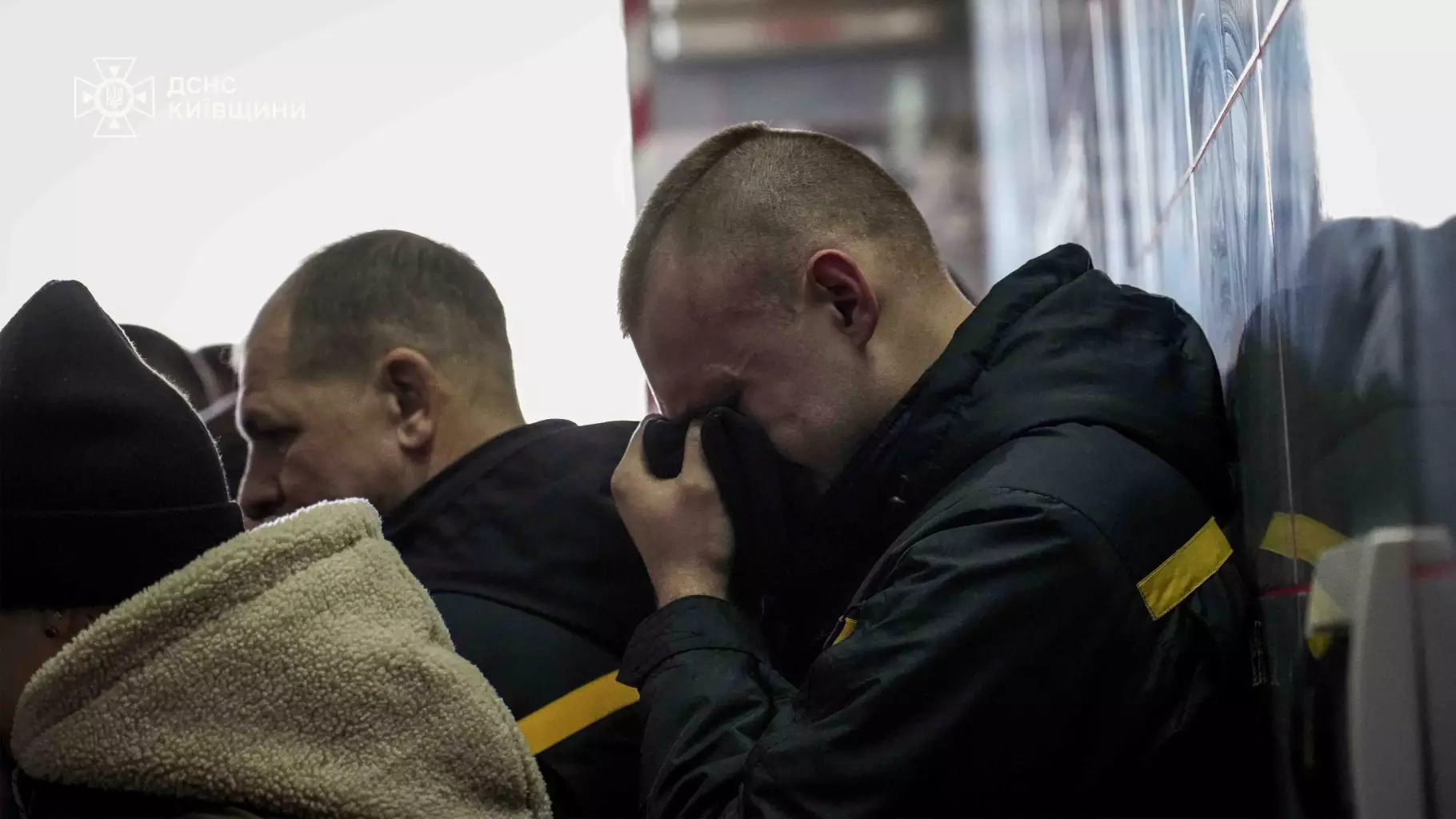 Рятувальники ДСНС України під час прощання з колегою, один з них витирає сльози, підтримуючи один одного