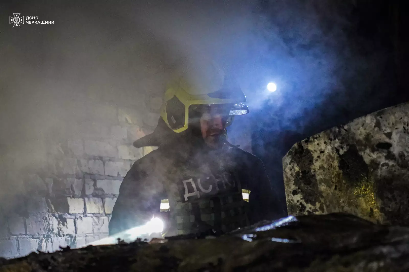 Рятувальник у захисному спорядженні працює серед диму в зруйнованій будівлі після обстрілу