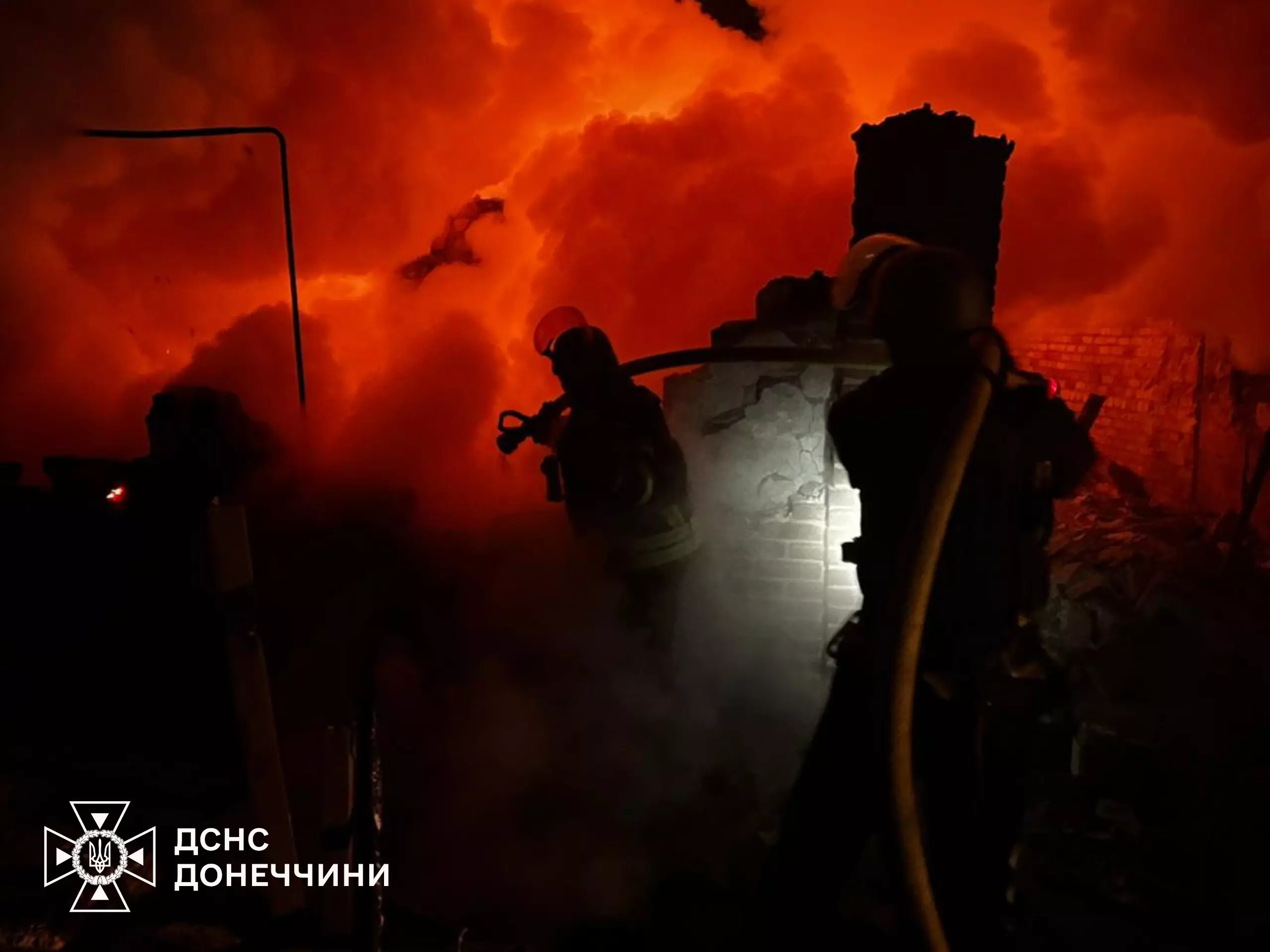 Рятувальники гасять пожежу вночі після обстрілу, густий дим і вогонь на фоні, видимі силуети людей