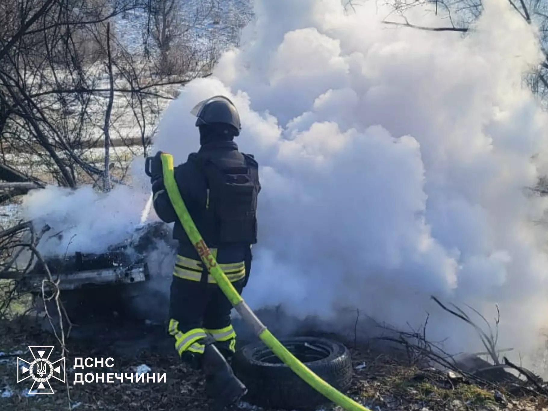 Рятувальник гасить пожежу після обстрілу, густий дим піднімається вгору, пошкоджене авто на фоні
