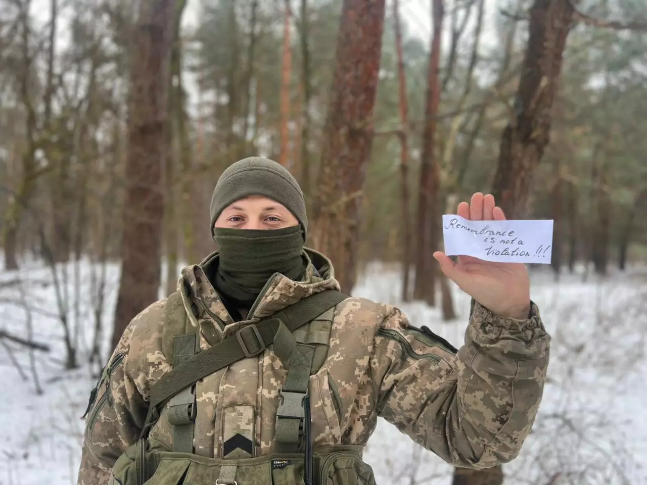 Військовослужбовець у камуфляжі тримає напис "Remembrance is not a violation" у зимовому лісі