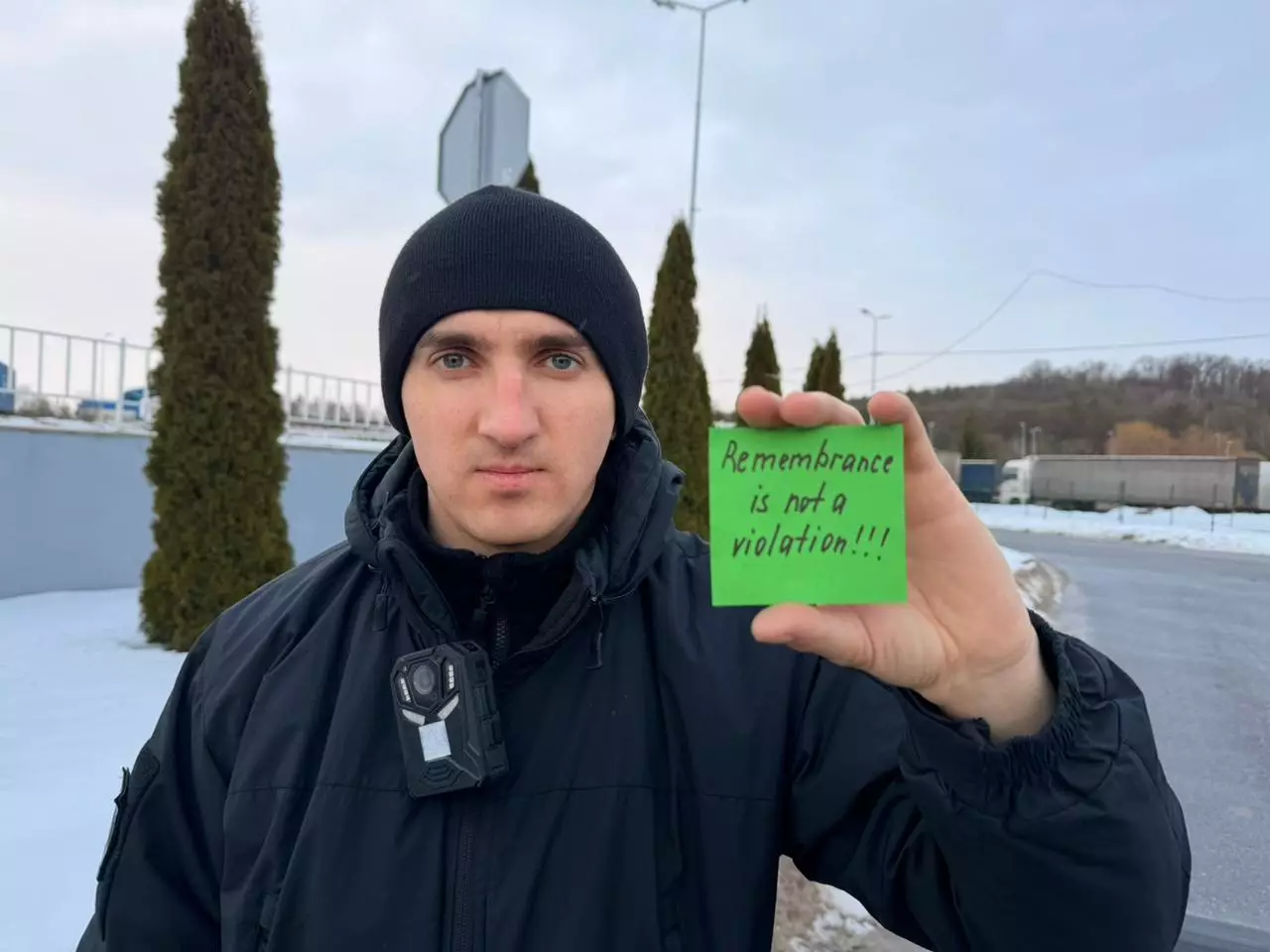 Чоловік у зимовій формі тримає зелений плакат з написом "Remembrance is not a violation